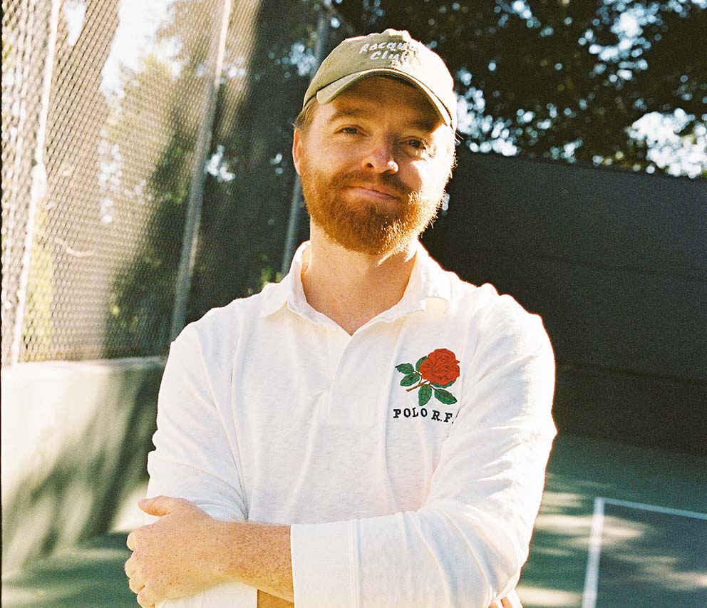 young man with red facial hair on a tennis court; past employee